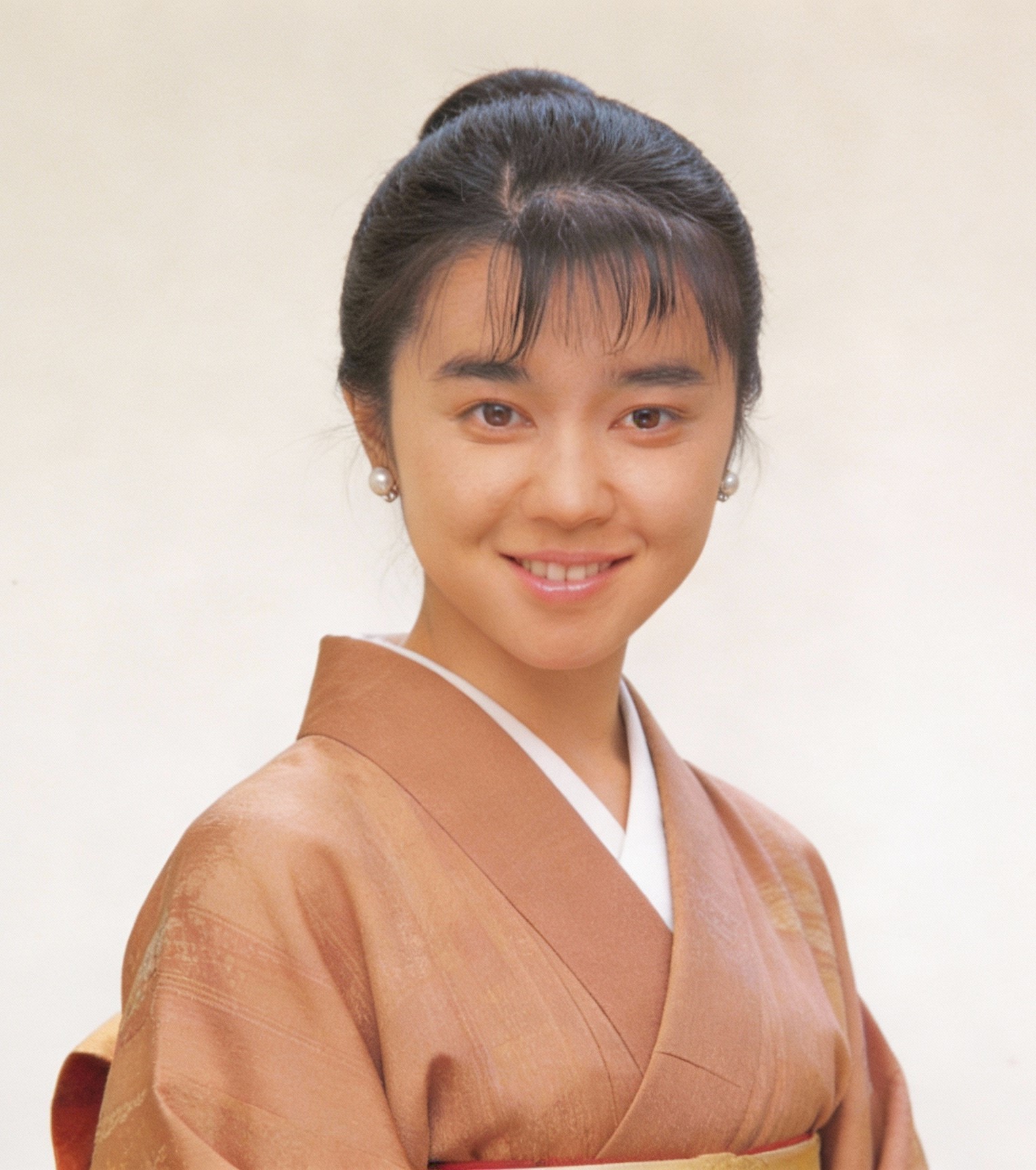 Young woman in a brown kimono smiling in a studio portrait.