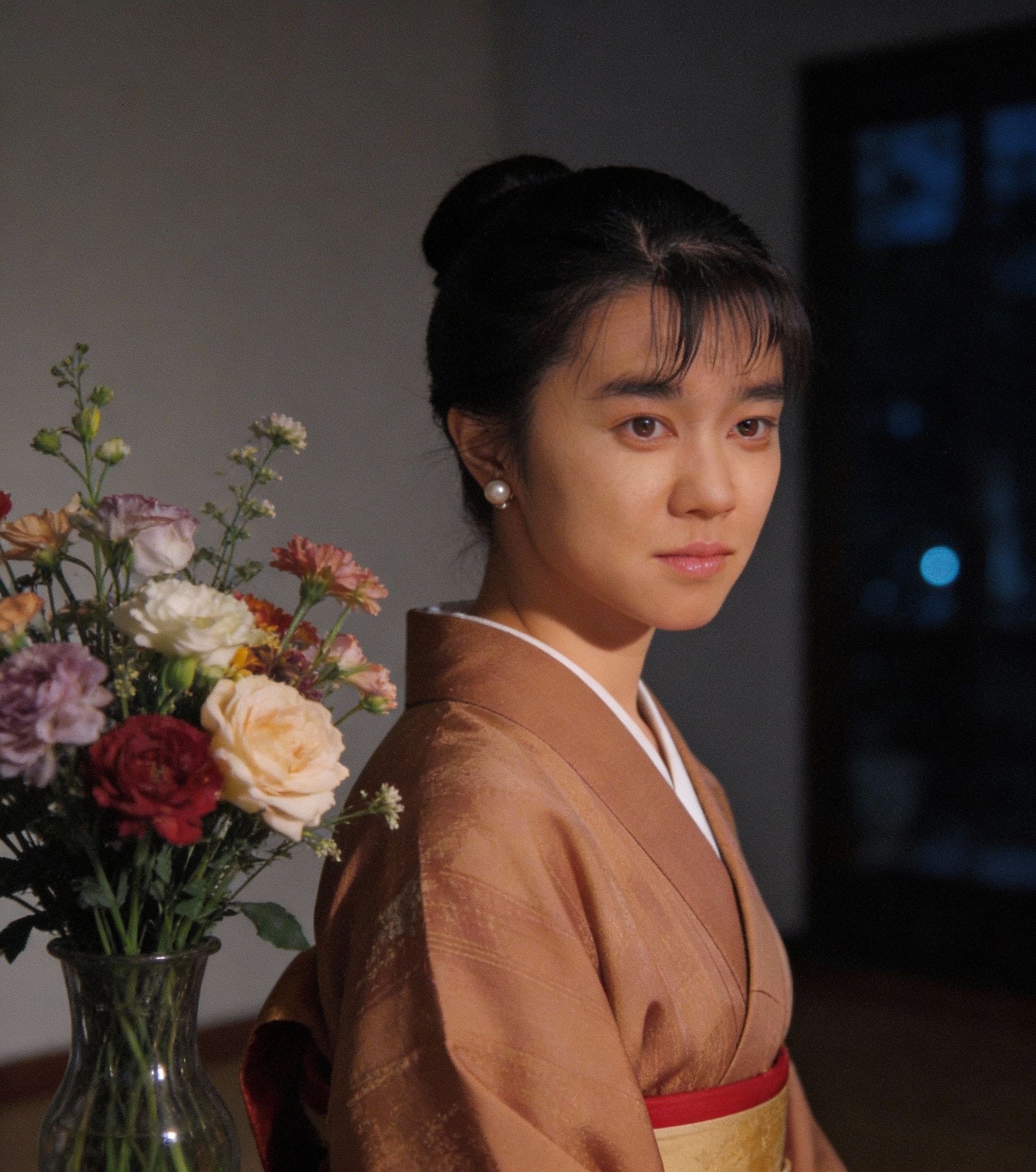Young woman in a peach kimono with a bouquet of colorful flowers beside her