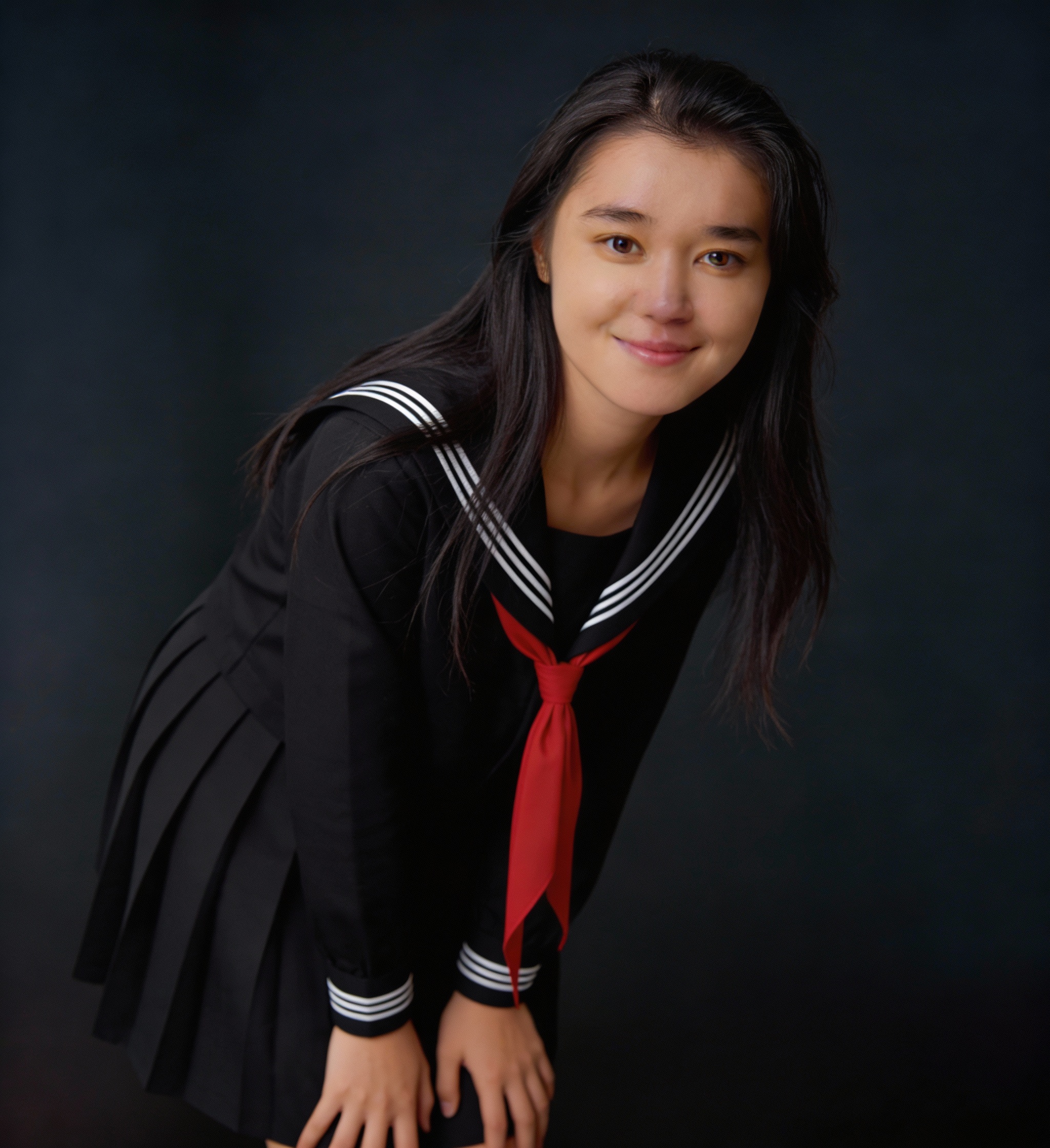Young woman in a black sailor-style school uniform with a red necktie, smiling gently.