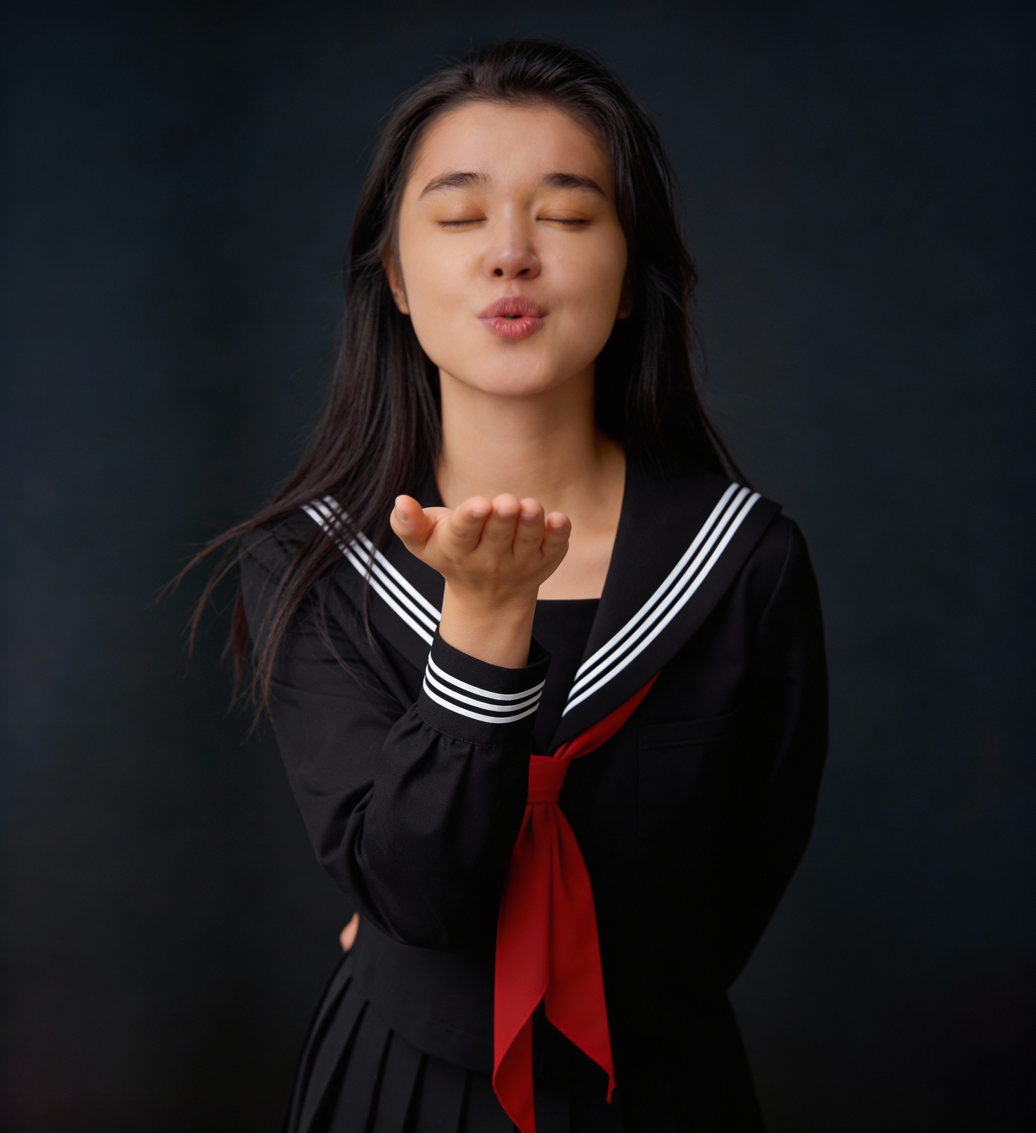 Young woman in a Japanese sailor-style school uniform blowing a kiss toward the camera