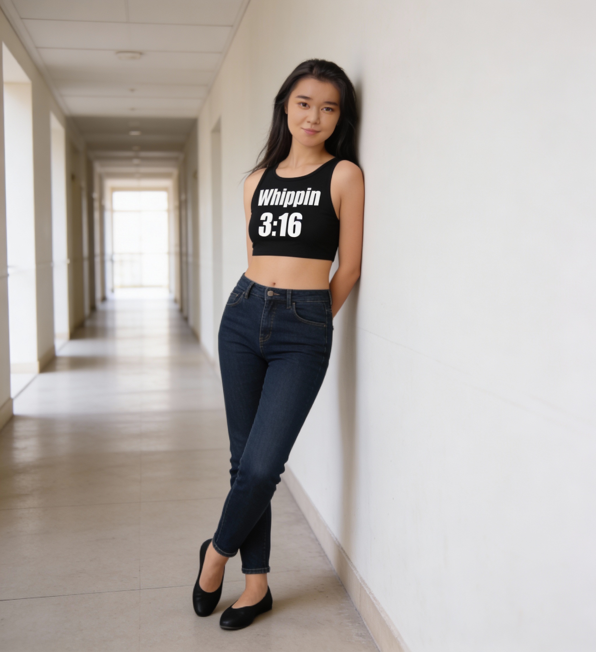 Woman in a black cropped tank top and dark jeans leaning against a hallway wall.