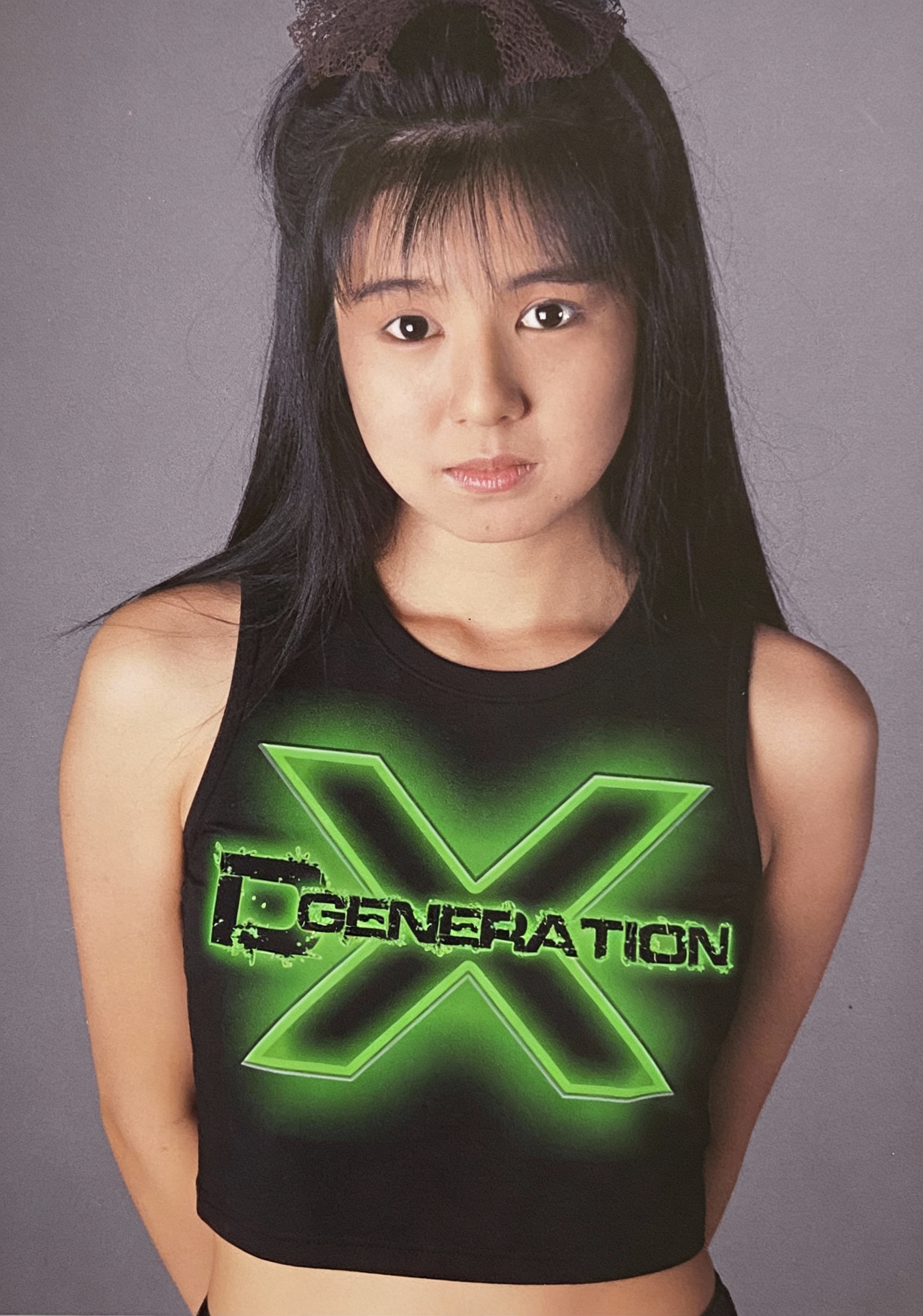 Young girl in a black cropped tank top with neon green XGENERATION graphic on a gray studio backdrop.