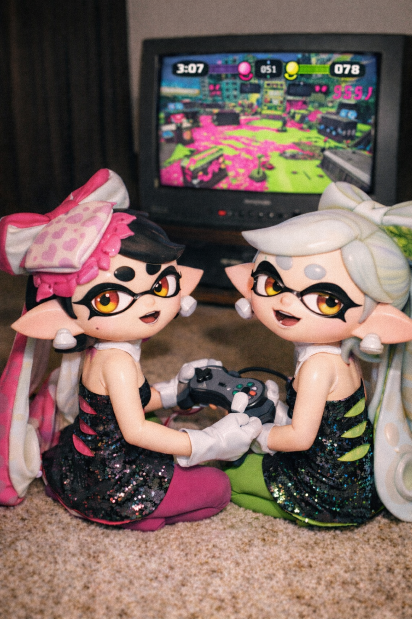 Two Splatoon-inspired plush dolls in glittery outfits playing a video game on a retro TV.